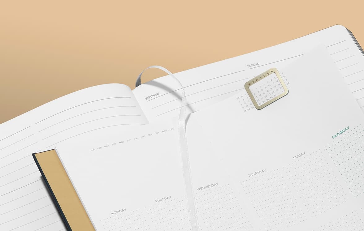 A close up image of two open perpetual planners placed on top of each other with a calendar clip and a ribbon page marker.