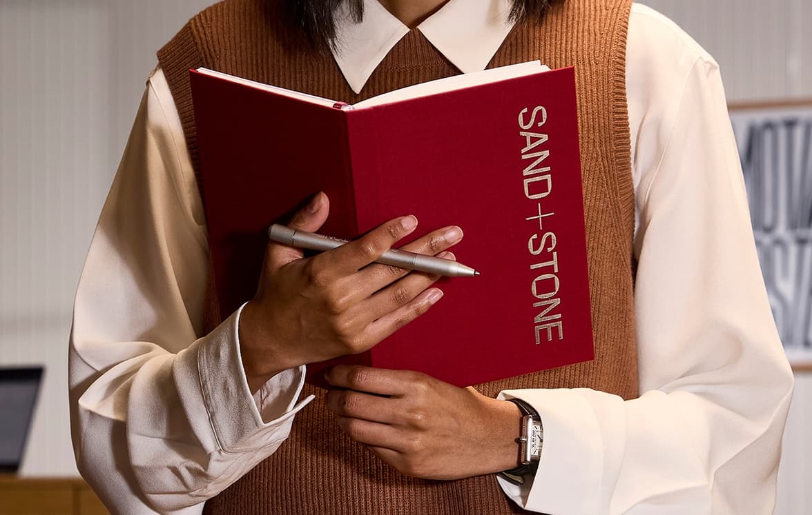 A person holding an open perpetual planner in front of them with a pen in one hand.