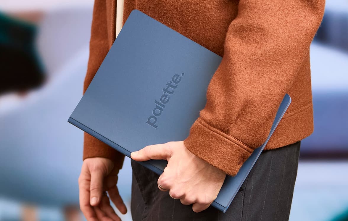 A person holding a blue softcover planner with one arm on their side.