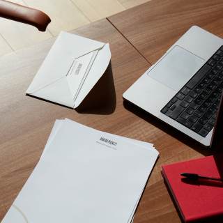 Letterheads, notebook, envelope and a laptop displayed on a desk