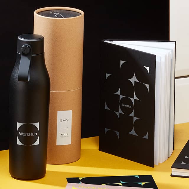 Custom black bottle next to its packaging and a custom black notebook