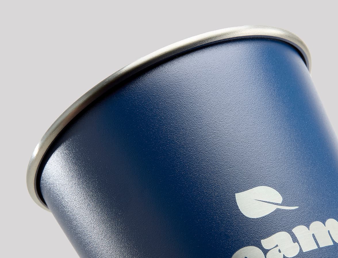 A close-up, slightly angled shot of the top half of a dark blue, matte-finish cup with a silver-colored rim, against a plain light gray background.