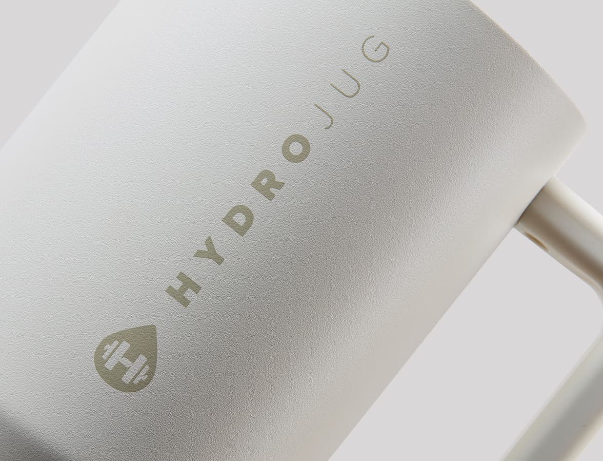 A close-up, slightly angled shot of a white matte mug. The words HYDROJUG TRAVELLER are debossed into the Tumbler