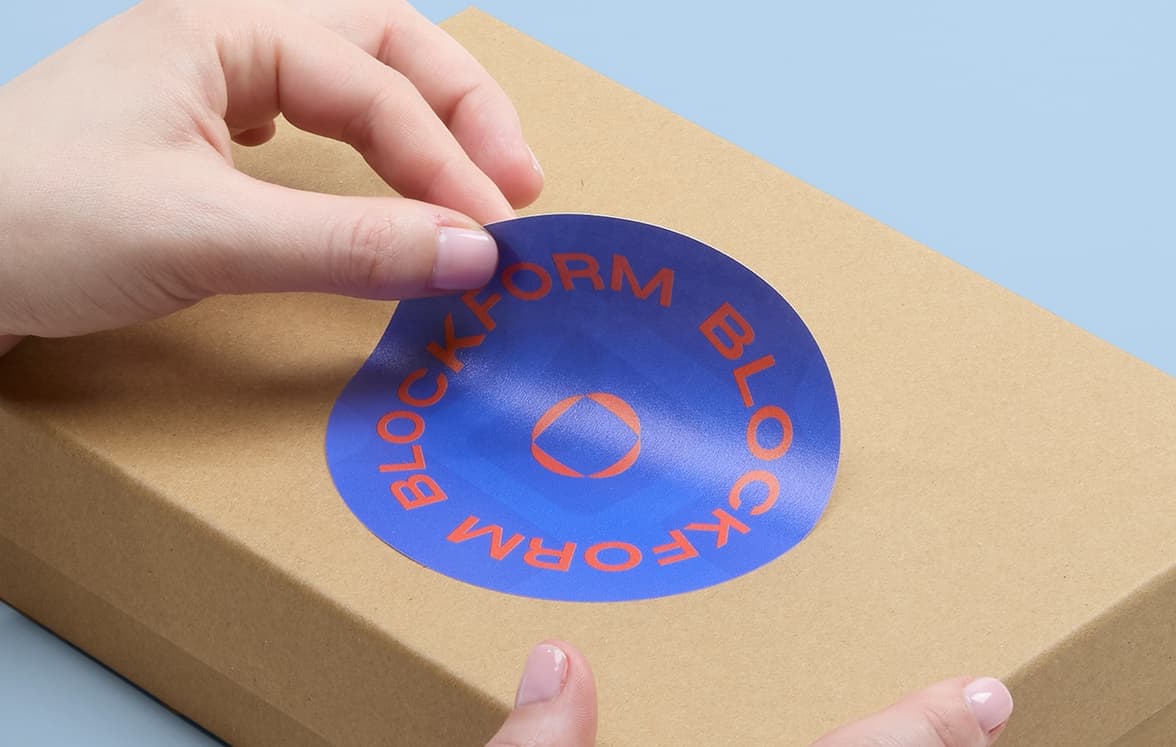 A hand placing a customized round matte paper sticker on a cardboard box.